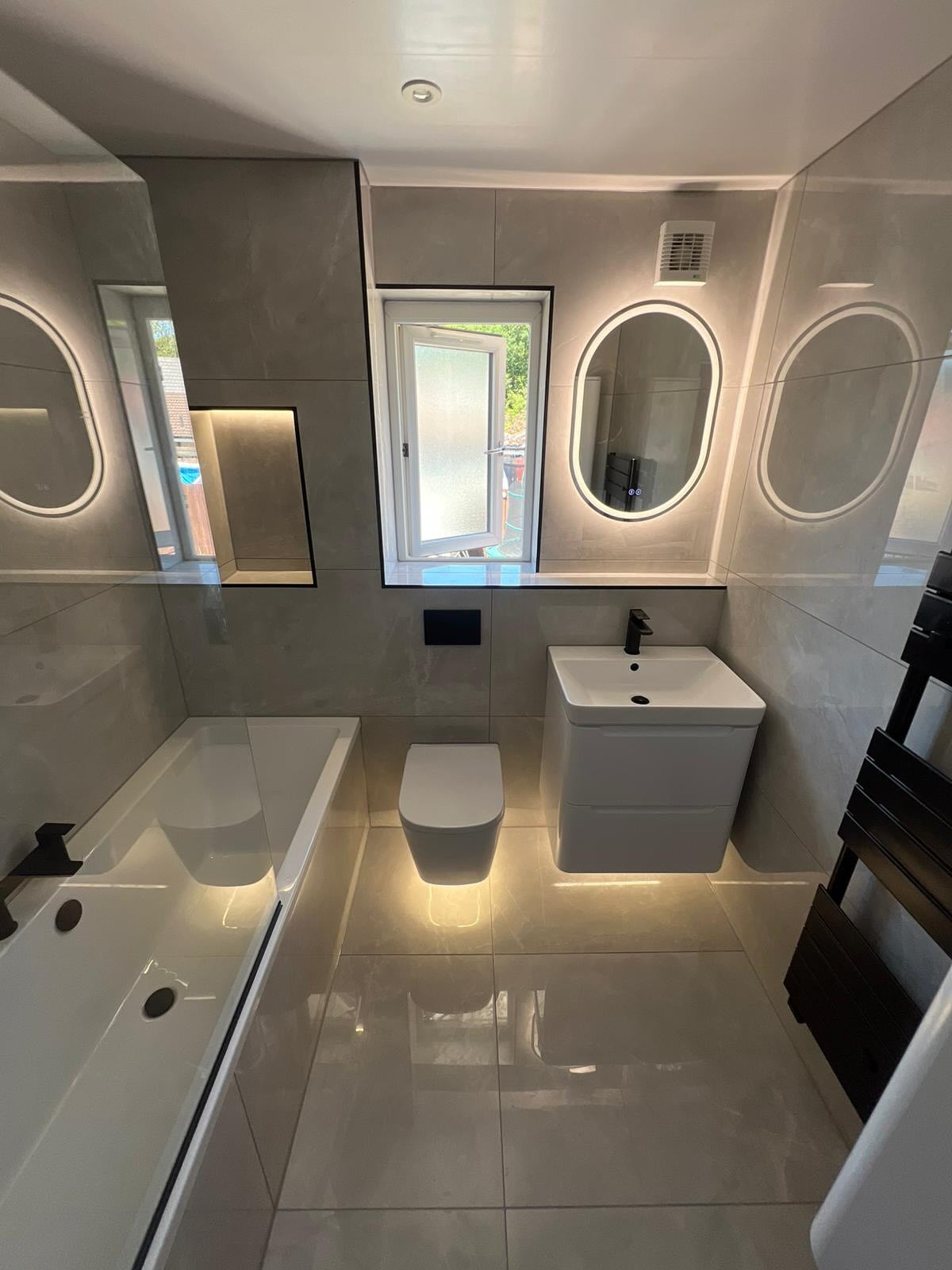 Family bathroom with oval backlit mirrors and black fittings, fitted by CDM